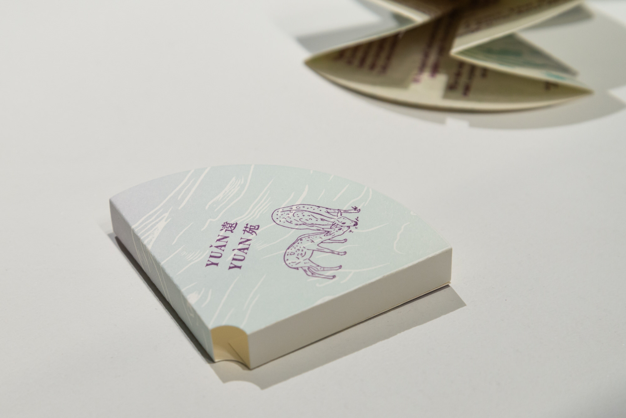 Cover sleeve for artist's book, printed in pale jade and lavender with an image of two deer grazing in deep violet