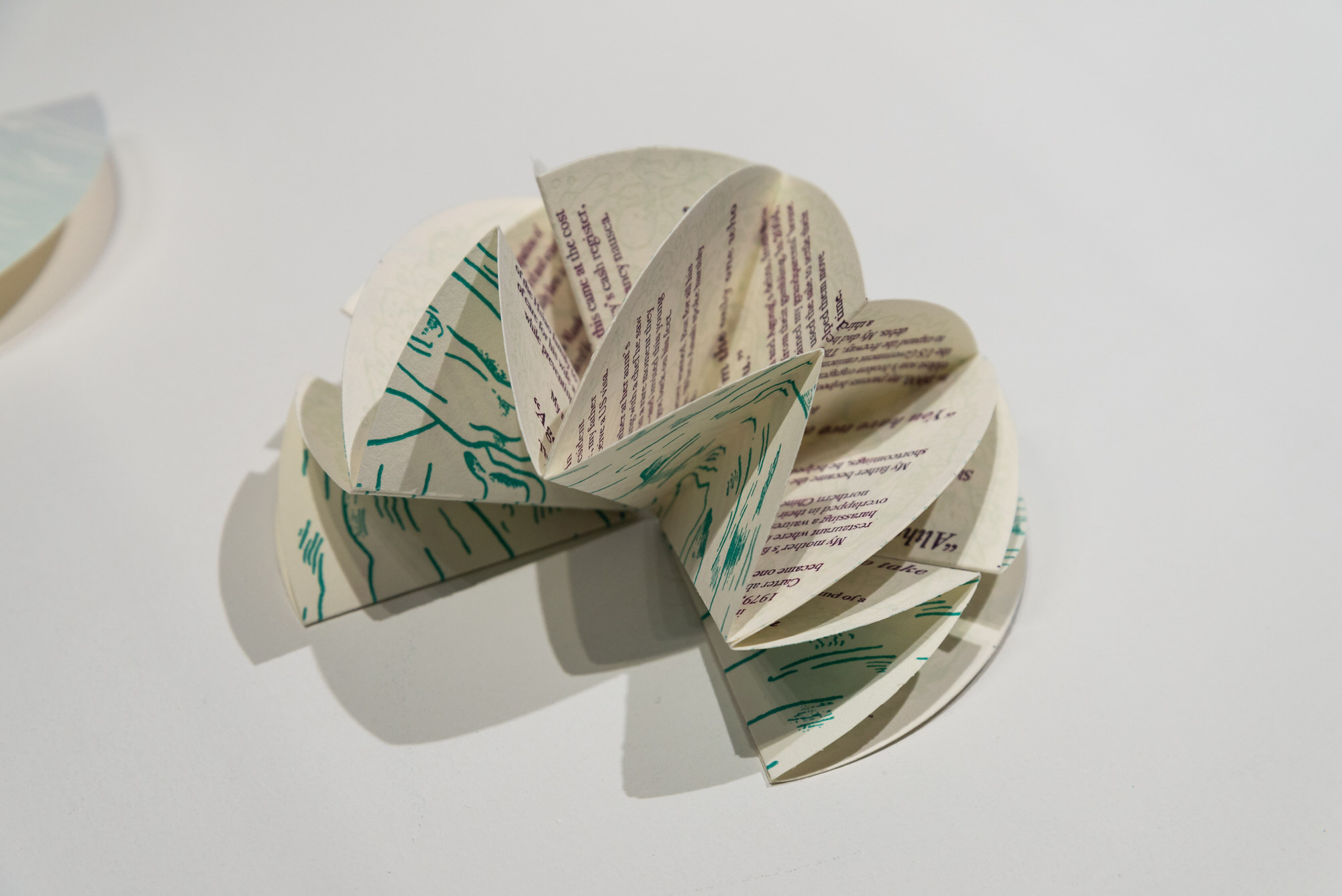 Artist's book fanned open resembling a flower, deep violet text visible through pages